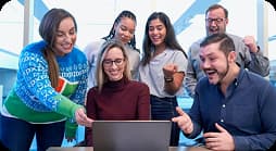 Grupo de compañeros de trabajo sonriendo mientras observan una computadora portátil