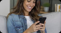 Mujer sonriendo mientras utiliza su teléfono celular sentada en un sofá