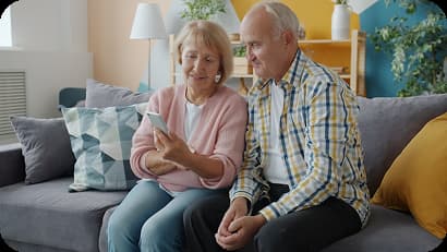 Pareja de adultos mayores sentados en un sofá mientras observan juntos un teléfono celular