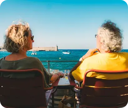 Pareja de adultos mayores sentada frente al mar disfrutando de la vista.