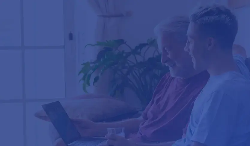 Hombre mayor y joven sonrientes usando una computadora portátil en la sala de estar.