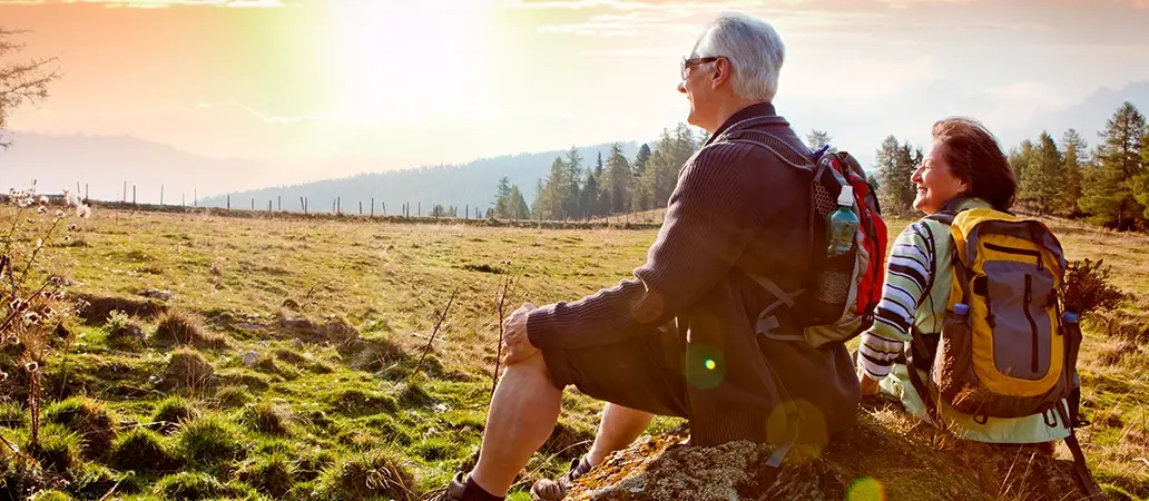 Pareja de adultos mayores con mochilas disfrutando de la vista en un paisaje natural al atardecer