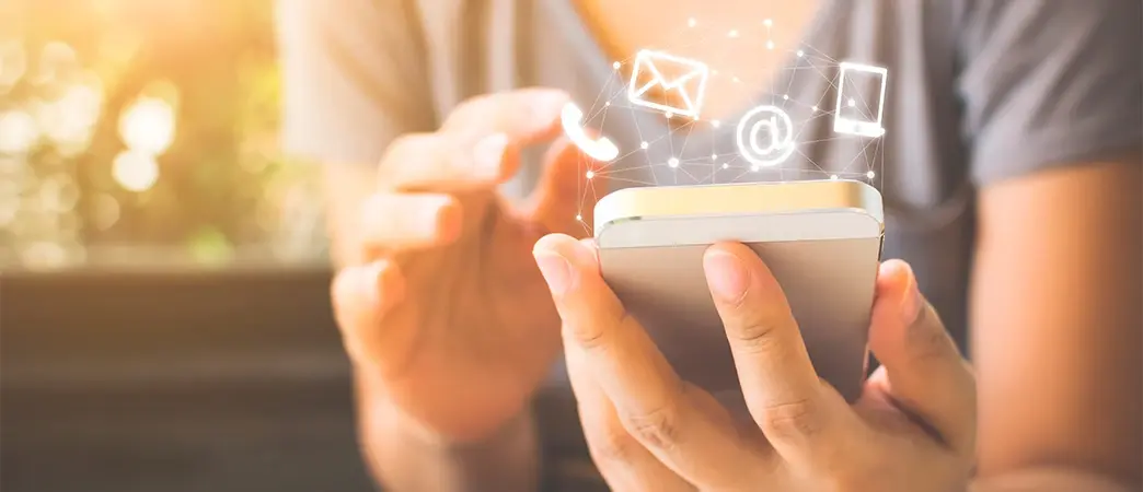 Persona usando un teléfono móvil con íconos digitales flotando sobre la pantalla, representando comunicación digital.