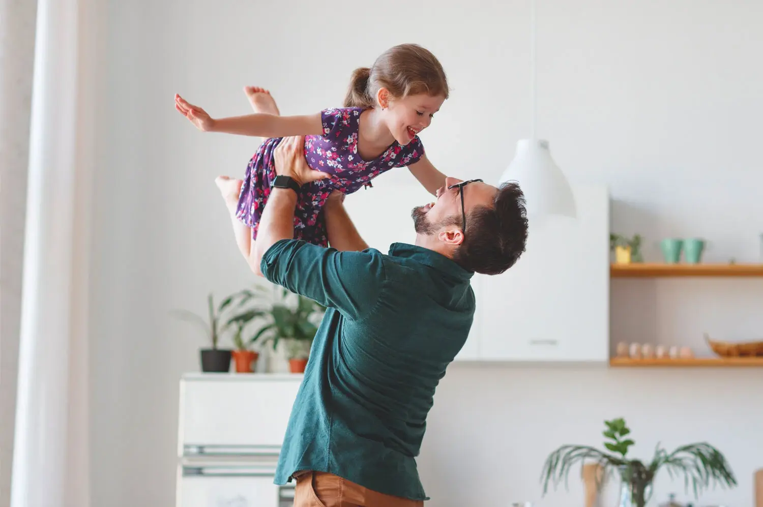 Padre levantando en brazos a su hija pequeña mientras sonríen en casa
