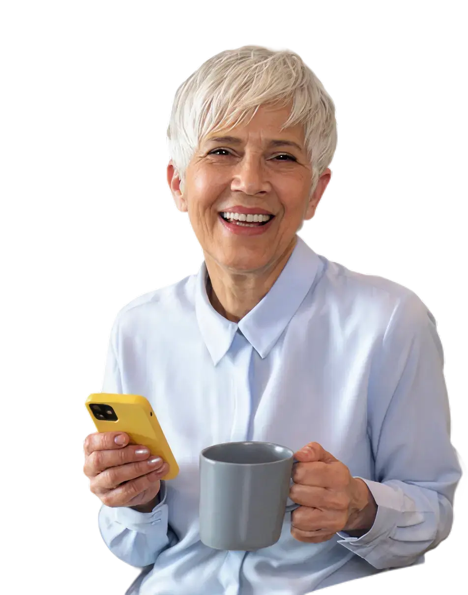Mujer adulta mayor sonriendo mientras sostiene un teléfono celular y una taza.