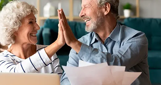 Pareja de adultos mayores sonriendo y chocando las manos en señal de celebración