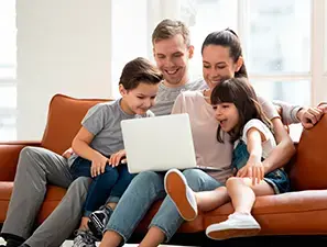 Familia con dos hijos sentados en un sofá, viendo una laptop y riendo juntos.