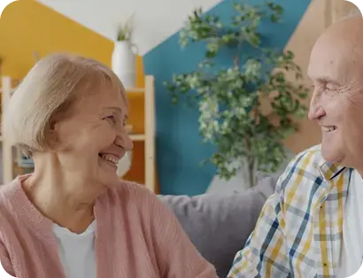 Pareja de adultos mayores sonriendo y mirándose en la sala de su casa.