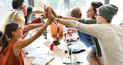 Grupo de jóvenes en una oficina celebrando con un gesto de manos unidas