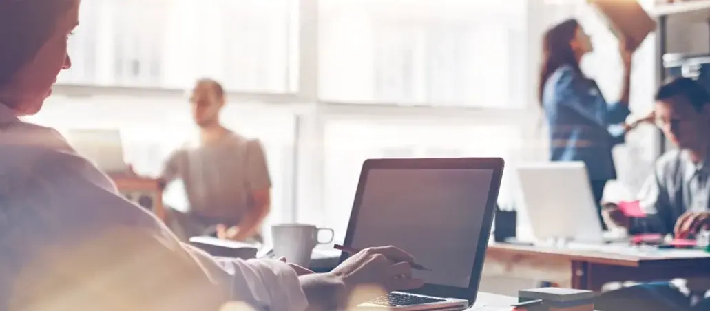 Personas trabajando en una oficina con computadoras portátiles y luz natural entrando por las ventanas.