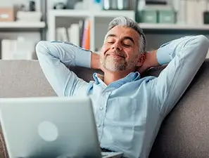 Hombre relajado con los ojos cerrados, descansando con una laptop sobre sus piernas.