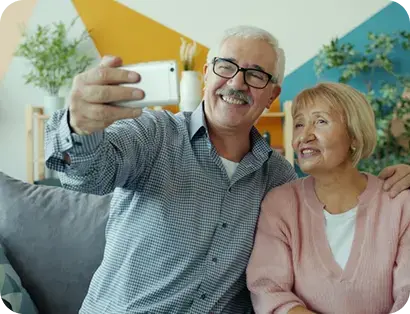 Pareja de adultos mayores sonriendo mientras se toma una selfie en casa.