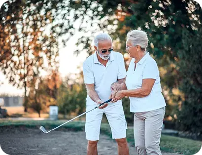 Pareja de adultos mayores practicando golf al aire libre.