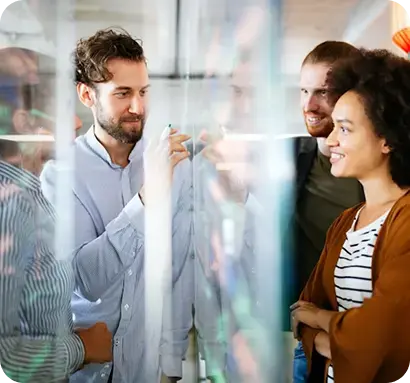 Equipo de trabajo compartiendo ideas y escribiendo en una pizarra de vidrio.